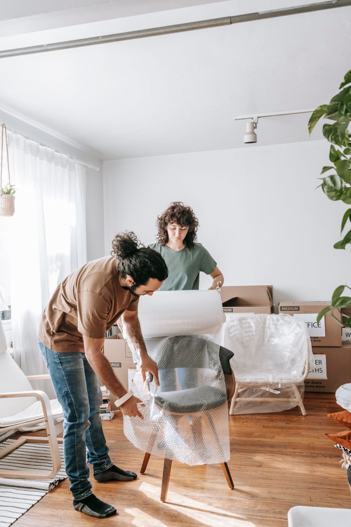 Mastering the First Impression: Your intriguing post title goes here A couple busy wrapping a chair for their move. Bright and organized indoor setting.
